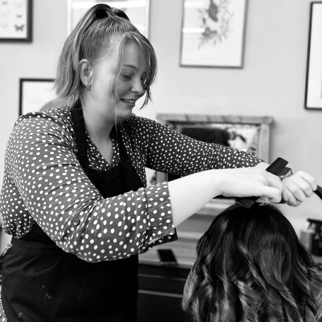 A girl in a polka dot top cutting a lady\x27s hair.