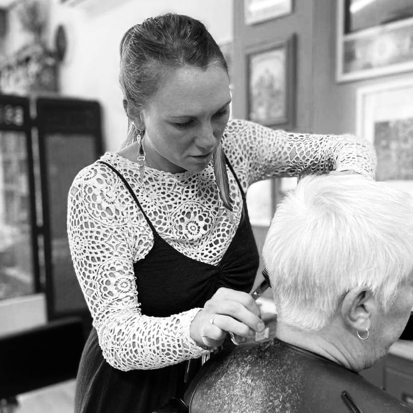 A girl wearing a white top trimming the hair of a lady.