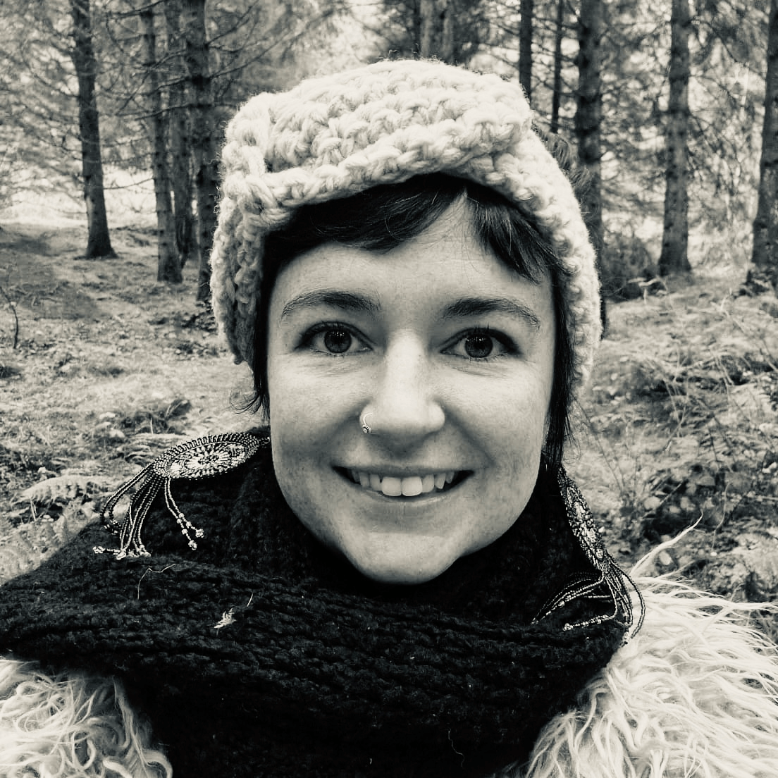 A girl smiling into the camera in the woods.